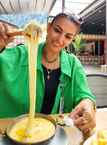 Uzungöl’de kuymak yerken uzayan peynirli kuymağı uzatan kadın.