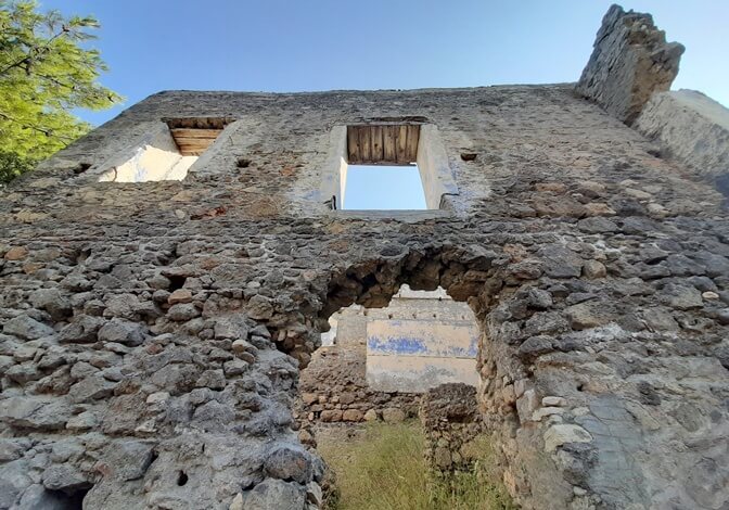 Kayaköy (Levissi)’de kemerli girişi ve boş pencereleriyle ayakta kalan taş bir evin ön cephesinden yukarıya bakış.
