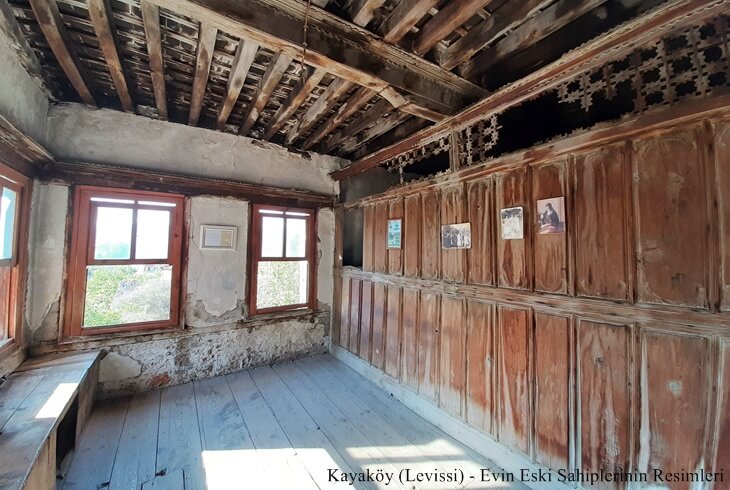 Kayaköy (Levissi)’de restore edilmiş bir evin içi, duvarda eski sahiplerinin fotoğraflarıyla ahşap mimari detaylar.