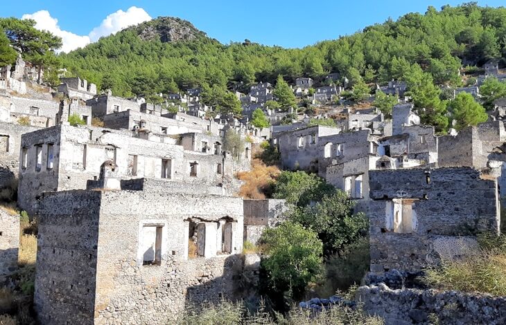 Fethiye Kayaköy'de terk edilmiş taş evler ve arka planda yeşil orman.