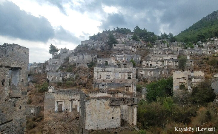 Kayaköy (Levissi)’de tepelere yayılmış terk edilmiş taş evler, bulutlu bir gökyüzü altında.