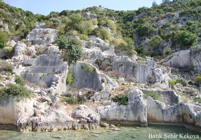Batık Şehir Kekova’da yamaç boyunca sıralanmış antik taş yapılar ve deniz kenarında suya yakın kalıntılar