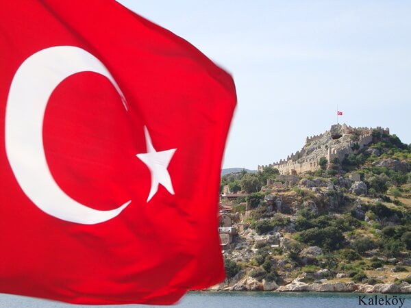 Kaleköy’de dalgalanan Türk bayrağı ve arka planda Simena Kalesi'nin taş surları