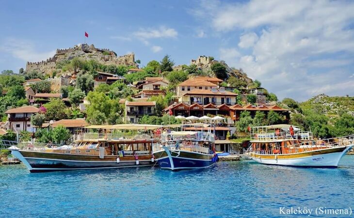 Kaleköy (Simena) kıyısında demirlemiş tekneler, taş evler ve tepeye kurulmuş tarihi kale manzarası