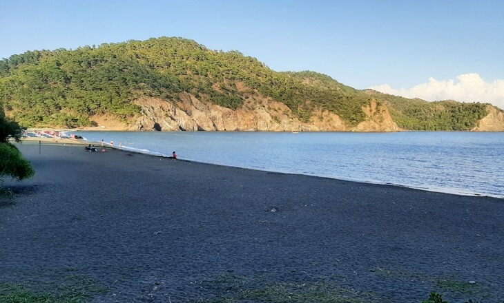 Fethiye’de yer alan İnlice Plajı’nın siyaha yakın renkli kumu ve sakin koy manzarası