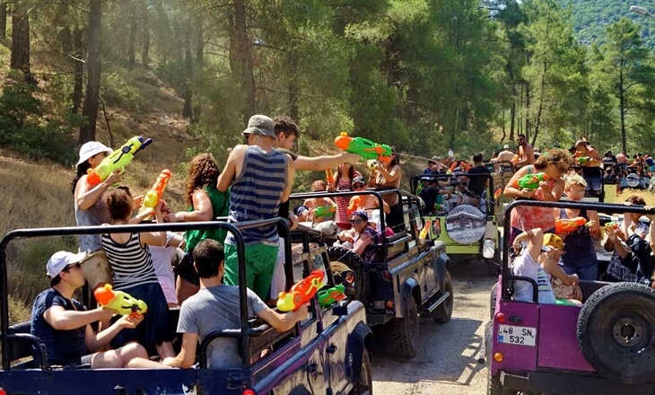 Orman içinde jeep safari turunda su tabancalarıyla eğlenen turist grubu