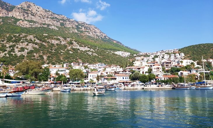 Kaş limanında tekneler, kıyı yerleşimi ve arka planda yükselen dağ manzarası