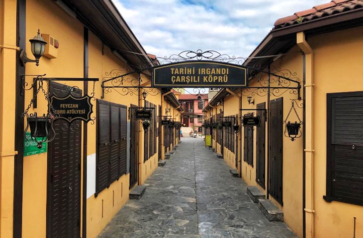 Bursa Irgandı K&ouml;pr&uuml;s&uuml; &ccedil;arşı girişi, sarı duvarlı d&uuml;kk&acirc;nlar, taş d&ouml;şeli yol ve Osmanlı d&ouml;nemini hatırlatan nostaljik &ccedil;arşı atmosferi