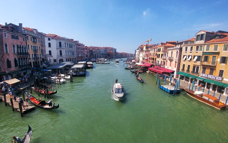 Venedik&rsquo;te Rialto K&ouml;pr&uuml;s&uuml;&rsquo;n&uuml;n &uuml;zerinden B&uuml;y&uuml;k Kanal manzarası, iki yanda sıralanan tarihi binalar, gondollar ve teknelerle şehrin canlı ticaret hattını g&ouml;steren g&ouml;r&uuml;n&uuml;m