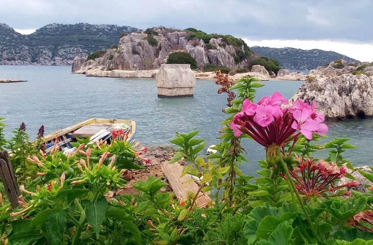 Kekova Batık Şehir – Likya kıyılarında deniz içindeki antik kalıntılar ve ön planda çiçeklerle süslü manzara