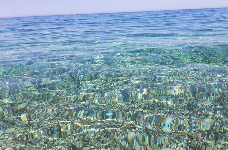 Olimpos Plajı’nda taşlık zemini gösteren berrak ve dalgasız deniz suyu