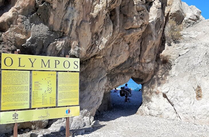 Olimpos Plajı'na girişte yer alan bilgilendirme tabelası ve kayaların arasından geçen doğal geçit