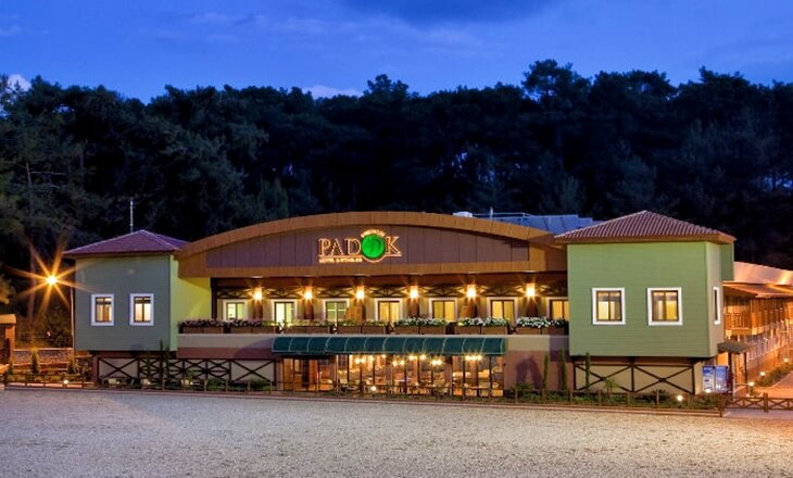 Gökova’daki Padok Premium Hotel & Stables, akşam saatlerinde ışıklarla aydınlatılmış modern ve doğal mimarili otel binası.