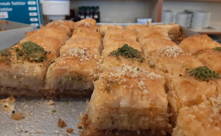 Alt text: Tepside servise hazır cevizli baklava dilimleri, üzeri antep fıstığı ve toz cevizle süslenmiş.