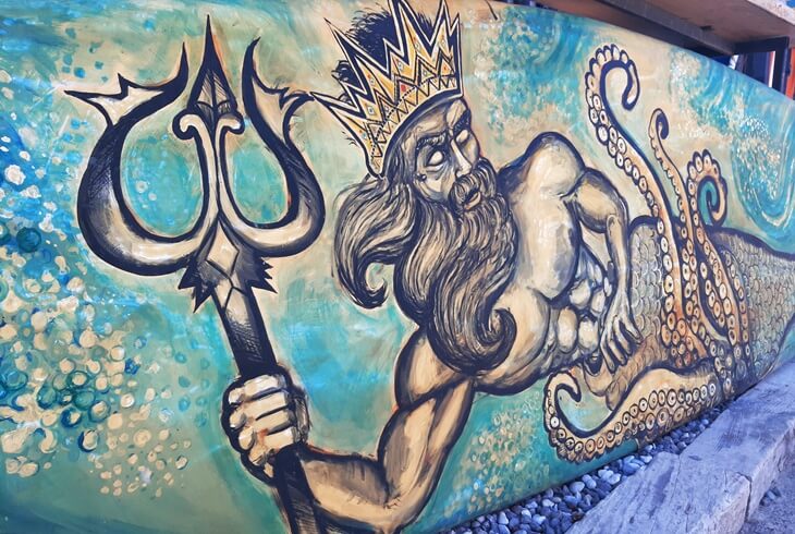 Selimiye&rsquo;de bir duvara &ccedil;izilmiş ta&ccedil;lı, &uuml;&ccedil; dişli mızrak taşıyan deniz tanrısı Poseidon fig&uuml;r&uuml;; ahtapot kuyruğu ve mavi-yeşil arka plan detaylarıyla dikkat &ccedil;ekici bir sokak sanatı &ouml;rneği.