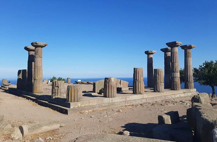 Assos Athena Tapınağı&rsquo;nın podiumu ve ayakta kalan Dor s&uuml;tunları, mavi g&ouml;ky&uuml;z&uuml; ve deniz manzarası.