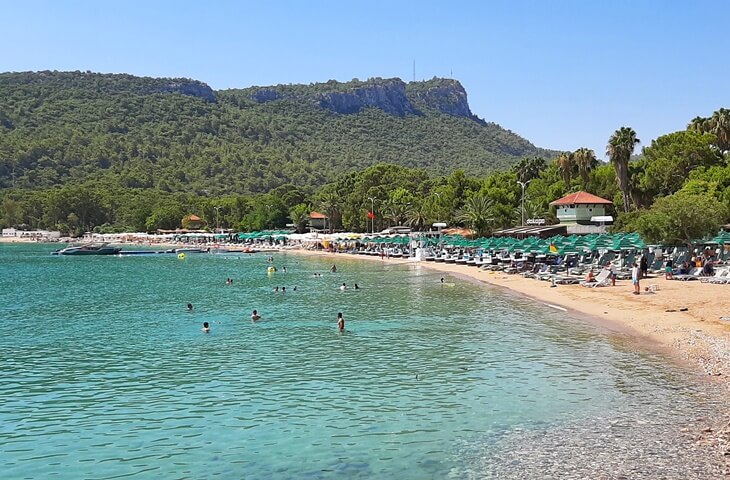 Antalya Kemer&rsquo;deki Ayışığı Plajı, berrak deniz, &ccedil;am ormanları ve şezlonglarla dolu sahil