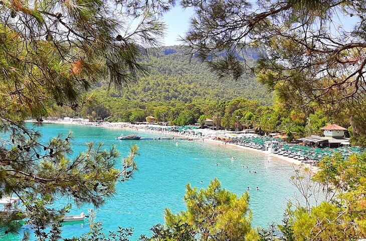 Antalya Kemer'de &ccedil;am ormanlarıyla &ccedil;evrili berrak deniz ve plaj, şezlonglar ve tatilcilerle dolu sahil g&ouml;r&uuml;nt&uuml;s&uuml;