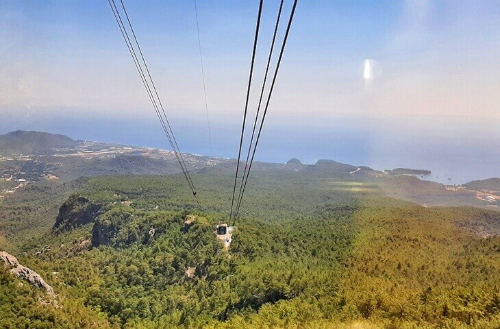 Olympos Teleferik kabini Tahtalı Dağı’na doğru yükselirken, aşağıda çam ormanları ve Akdeniz manzarası görülüyor