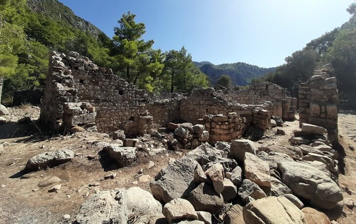 Olympos Antik Kenti’nde doğa içinde yer alan, taş duvarlarla örülmüş yıkık tarihi yapılar ve çevresinde dağlık ormanlık alan