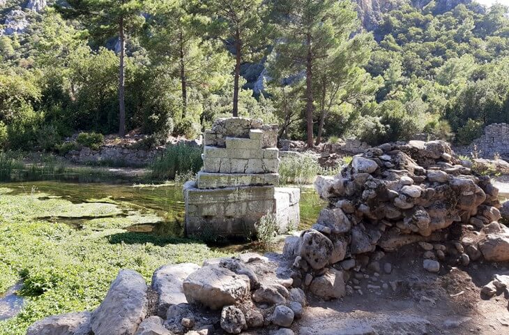 Olympos Antik Kenti’nde yer alan, Vespasianus Hamamı'na ait su kenarındaki taş yapı kalıntıları ve çevresindeki doğal bitki örtüsü