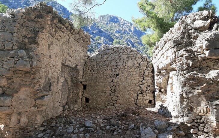 Olympos Antik Kenti’ndeki Batı Nekropol alanında yer alan taş duvarlı antik mezar yapıları ve çevresindeki ormanlık dağ manzarası