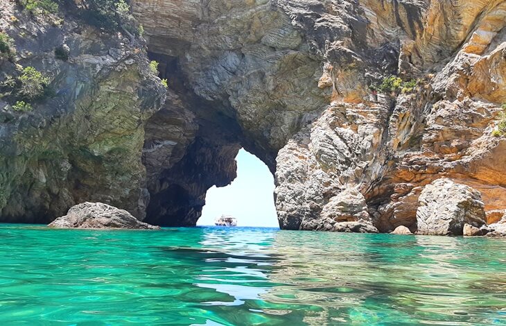 Gazipaşa’daki Delikdeniz Kral Koyu’nda kayaların oluşturduğu doğal kemer, berrak turkuaz su ve arka planda görünen bir tekne.