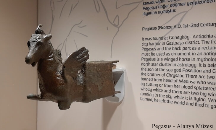 Alanya Müzesi’nde sergilenen, Antiochia ad Cragum kazılarından çıkarılmış bronz Pegasus figürü; arka planda İngilizce ve Türkçe bilgilendirme metniyle birlikte.