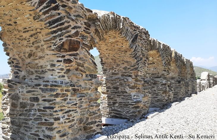 Gazipaşa Selinus Antik Kenti’nde restore edilmiş çok kemerli taş su kemeri yapısı, açık hava ve arka planda doğa ile birlikte geniş açıdan görüntülenmiş.