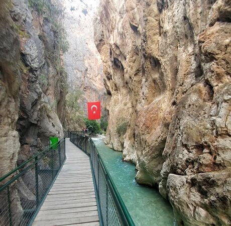 Saklıkent Kanyonu’nda kayalıklar arasında uzanan yürüyüş platformu ve derenin üstünde asılı Türk bayrağı