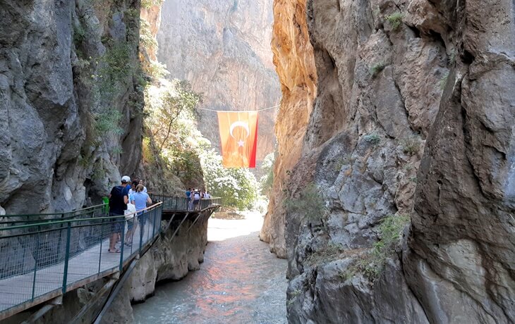 Saklıkent Kanyonu'nda yürüyüş platformunda ilerleyen turistler ve kanyonun ortasına asılmış Türk bayrağı