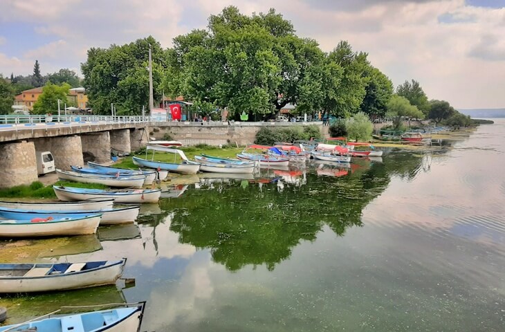 G&ouml;lyazı K&ouml;y&uuml;'nde g&ouml;l kıyısına bağlanmış sandallar ve arka planda tarihi taş k&ouml;pr&uuml;